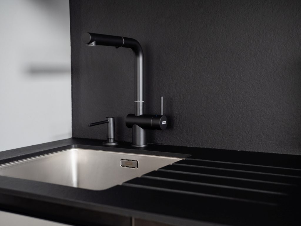 Pracovní deska a zádový panel jsou z kompaktu Grace Stone Black. Tento materiál je vysoce odolný i vodě, proto umožňuje využít dřezy se spodním umístěním a frézování okapových drážek přímo do desky.